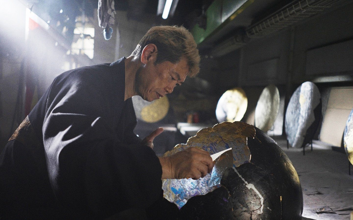 Metal leaf artist Hiroto Rakusho at work in his studio, applying leaf to a large dark sphere